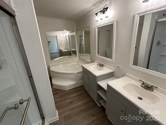 bathroom with a textured ceiling, ornamental molding, hardwood / wood-style floors, separate shower and tub, and vanity