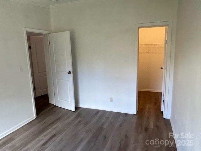 unfurnished bedroom with crown molding, a closet, a spacious closet, and dark hardwood / wood-style flooring