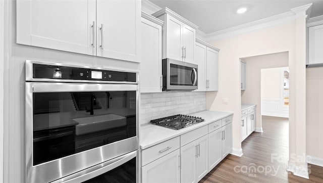 kitchen with stainless steel appliances, crown molding, dark wood-type flooring, white cabinetry, and tasteful backsplash