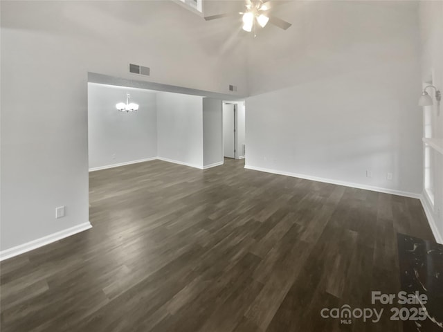 unfurnished living room featuring ceiling fan with notable chandelier, dark wood-type flooring, and a towering ceiling