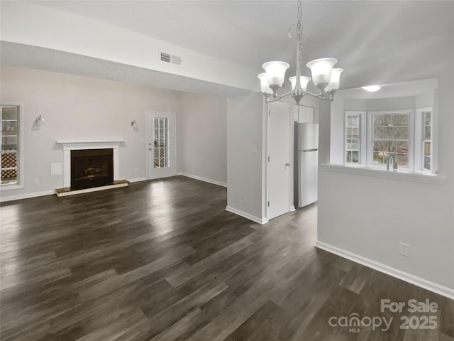 unfurnished living room featuring a notable chandelier and dark hardwood / wood-style floors