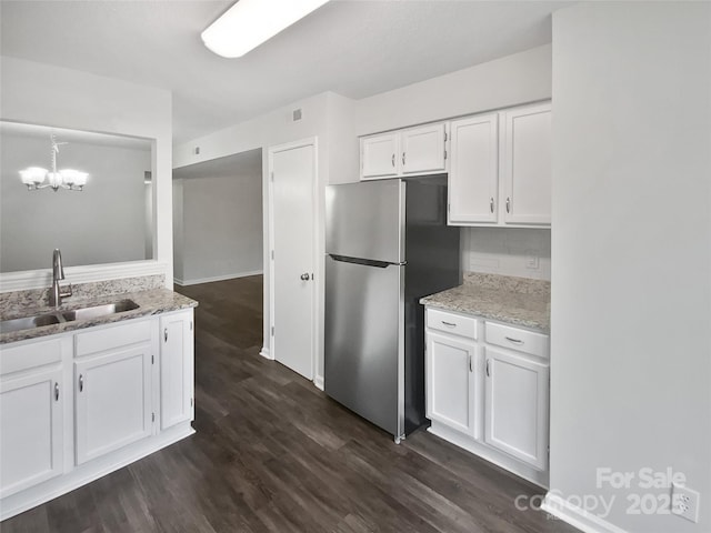 kitchen featuring dark wood-type flooring, a notable chandelier, white cabinetry, stainless steel refrigerator, and sink