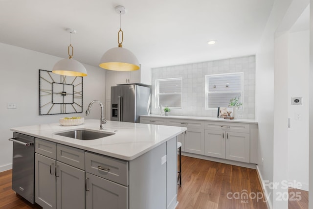 kitchen with pendant lighting, stainless steel appliances, an island with sink, sink, and light stone counters