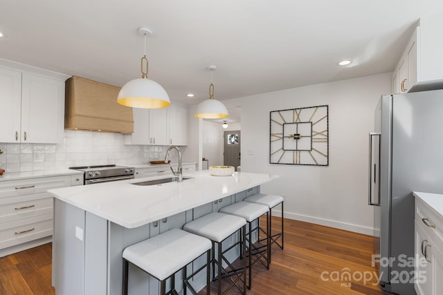 kitchen featuring premium range hood, white cabinetry, appliances with stainless steel finishes, a kitchen island with sink, and sink