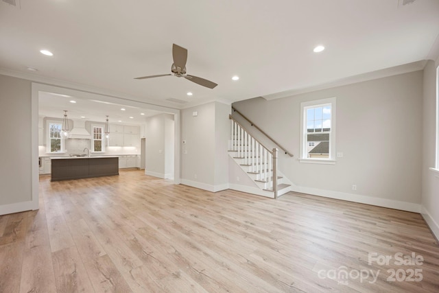 unfurnished living room featuring stairway, baseboards, light wood finished floors, a sink, and crown molding