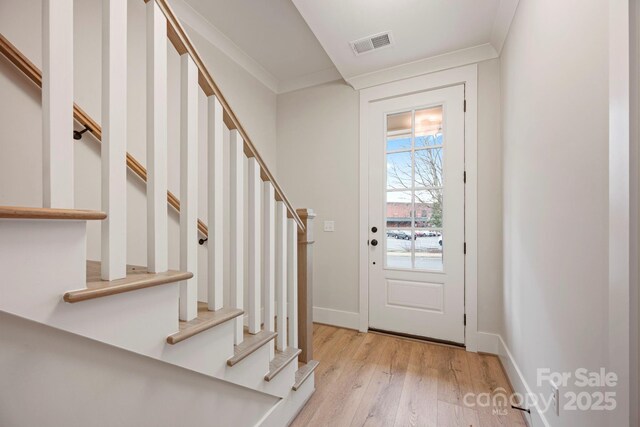 entrance foyer featuring visible vents, light wood-style flooring, ornamental molding, baseboards, and stairs