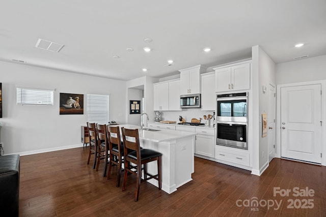 kitchen featuring a breakfast bar, sink, white cabinetry, a kitchen island with sink, and appliances with stainless steel finishes