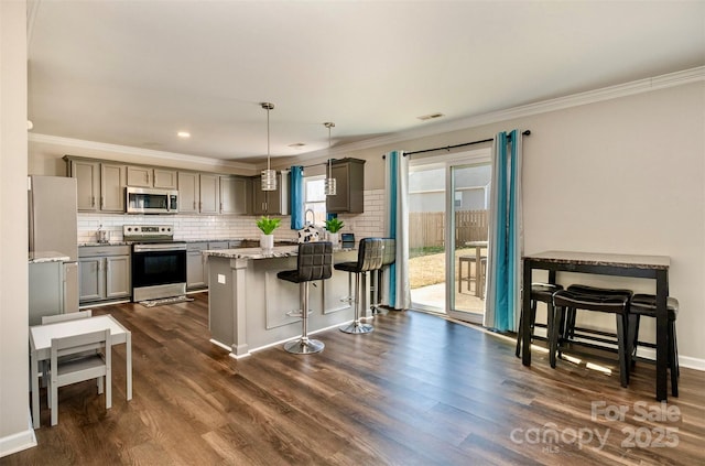 kitchen featuring pendant lighting, gray cabinets, appliances with stainless steel finishes, light stone counters, and decorative backsplash