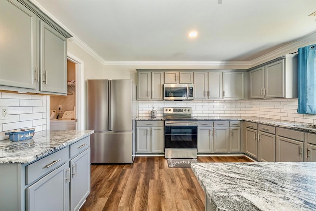 kitchen featuring stainless steel appliances, dark hardwood / wood-style flooring, light stone countertops, and washer and clothes dryer