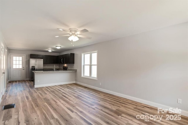 kitchen with kitchen peninsula, light stone countertops, stainless steel fridge, ceiling fan, and wood-type flooring