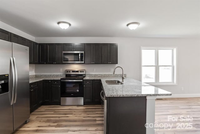 kitchen featuring appliances with stainless steel finishes, light wood-type flooring, light stone countertops, kitchen peninsula, and sink