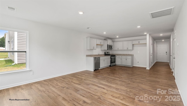 kitchen featuring light wood-type flooring, appliances with stainless steel finishes, white cabinets, and light stone countertops