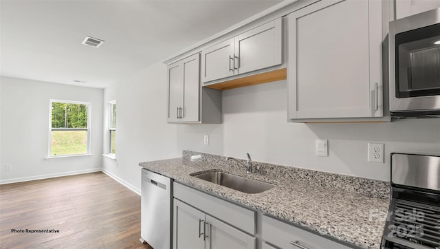 kitchen with appliances with stainless steel finishes, sink, light stone counters, and hardwood / wood-style flooring