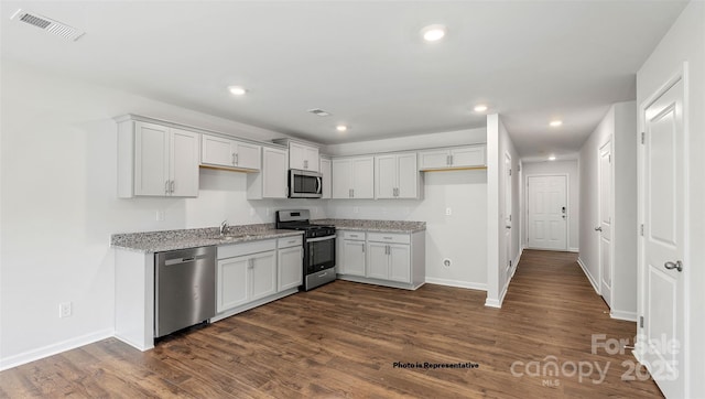 kitchen with light stone countertops, white cabinets, appliances with stainless steel finishes, sink, and dark hardwood / wood-style floors