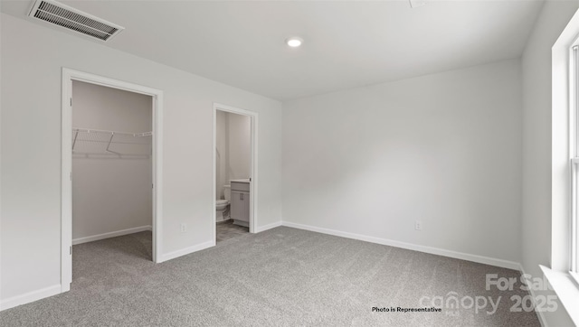 unfurnished bedroom featuring a spacious closet, a closet, light carpet, and ensuite bath