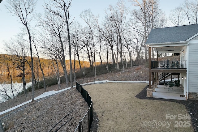 view of yard featuring a deck with water view, ceiling fan, and a patio area