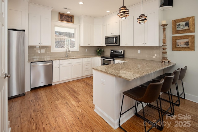 kitchen featuring pendant lighting, sink, appliances with stainless steel finishes, white cabinets, and kitchen peninsula