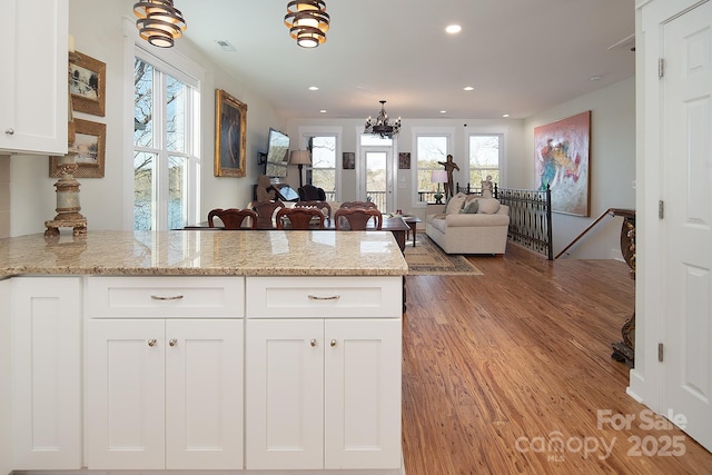 kitchen with a notable chandelier, light stone countertops, white cabinets, and light wood-type flooring