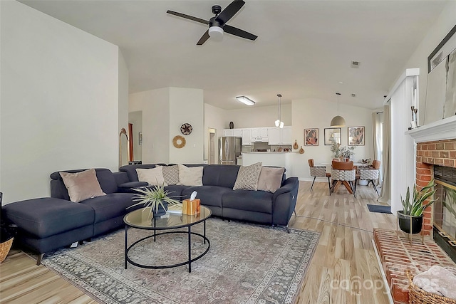 living room featuring light hardwood / wood-style floors, ceiling fan, a brick fireplace, and vaulted ceiling