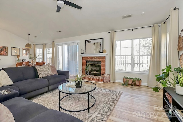 living room featuring a brick fireplace, light hardwood / wood-style flooring, ceiling fan, and vaulted ceiling