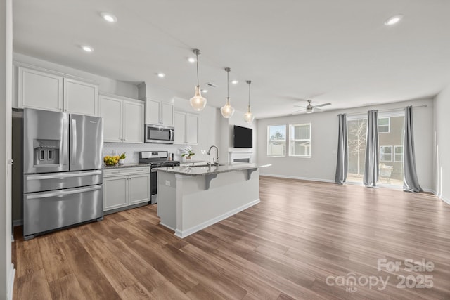 kitchen featuring appliances with stainless steel finishes, a kitchen bar, an island with sink, backsplash, and stone counters