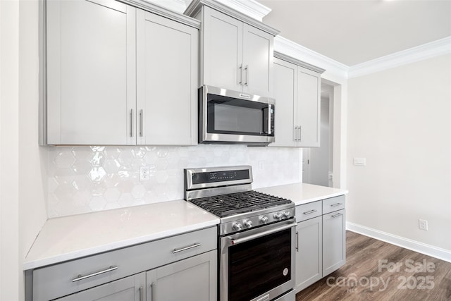 kitchen with stainless steel appliances, ornamental molding, decorative backsplash, dark hardwood / wood-style flooring, and gray cabinetry