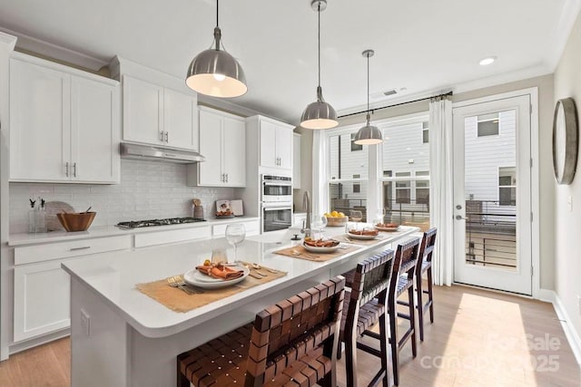 kitchen featuring hanging light fixtures, an island with sink, a kitchen bar, white cabinetry, and appliances with stainless steel finishes