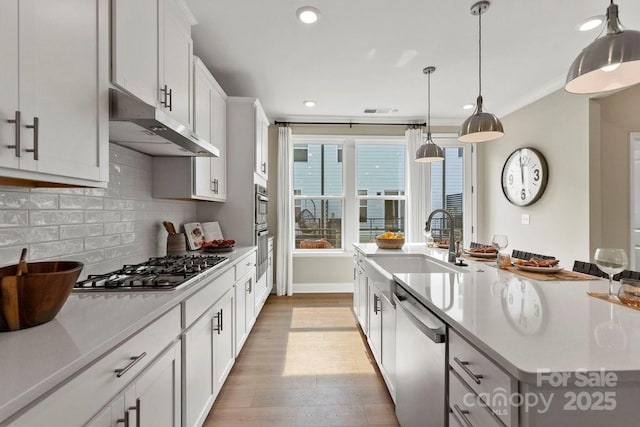 kitchen featuring appliances with stainless steel finishes, hanging light fixtures, sink, white cabinets, and tasteful backsplash