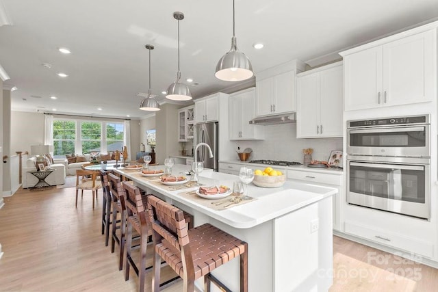 kitchen featuring a breakfast bar, stainless steel appliances, decorative light fixtures, and a center island with sink