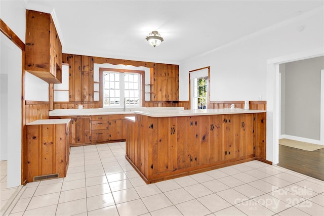 kitchen featuring plenty of natural light, light tile patterned floors, crown molding, and kitchen peninsula