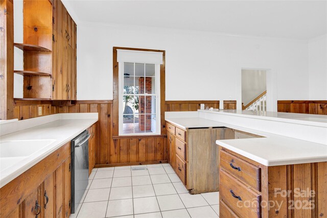 kitchen with light tile patterned flooring, stainless steel dishwasher, wooden walls, and sink