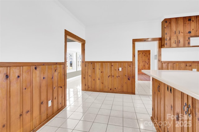 corridor with wood walls, ornamental molding, and light tile patterned flooring