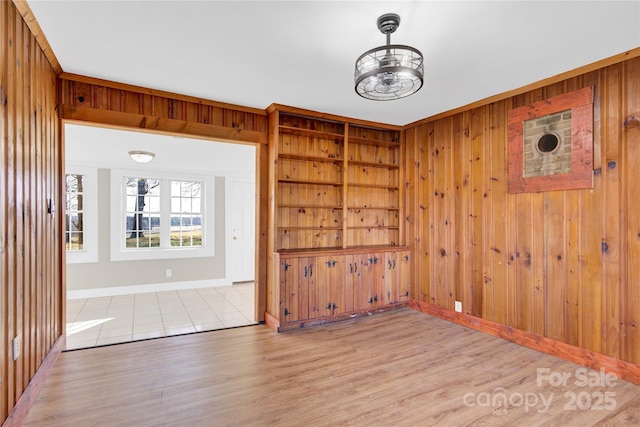 unfurnished room featuring light hardwood / wood-style floors, built in features, and wood walls