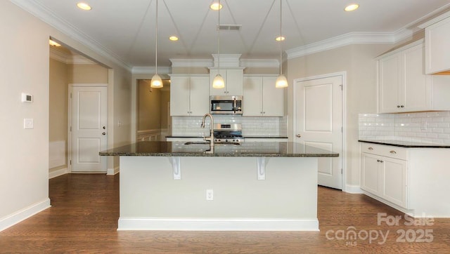 kitchen with stainless steel appliances, white cabinets, an island with sink, and sink