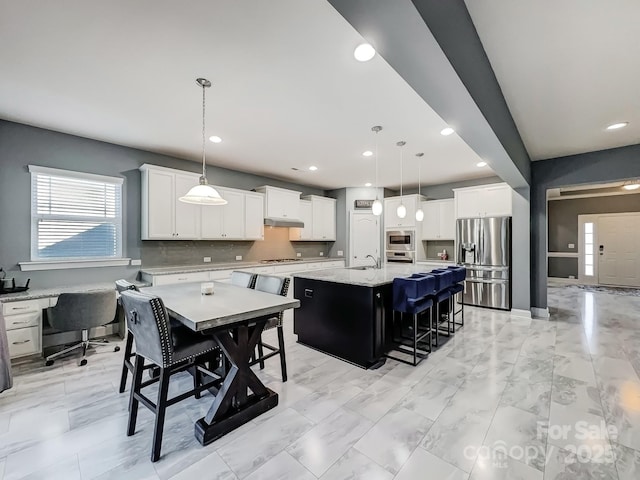 kitchen featuring white cabinets, hanging light fixtures, appliances with stainless steel finishes, and an island with sink