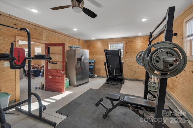 workout room with ceiling fan and wooden walls