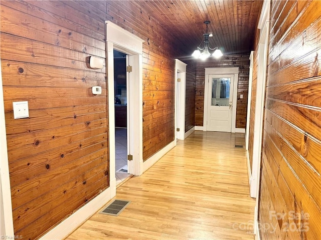 corridor with wood ceiling, wood walls, and a notable chandelier