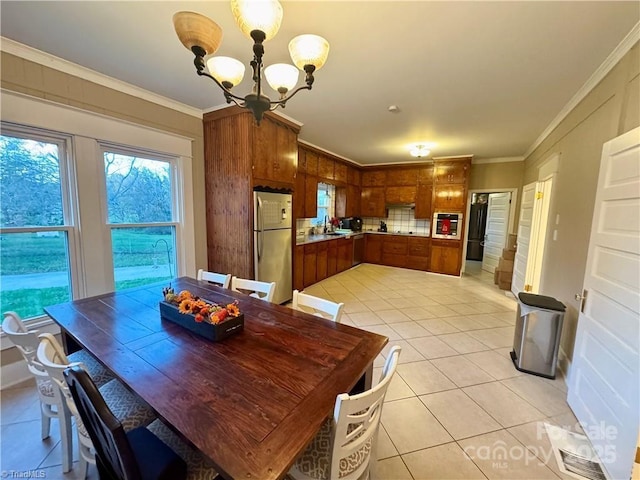 dining area with sink, light tile patterned floors, ornamental molding, and a notable chandelier