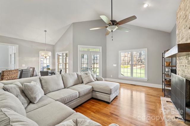 living room featuring ceiling fan, a fireplace, light hardwood / wood-style floors, high vaulted ceiling, and french doors