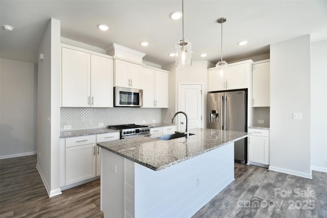 kitchen featuring premium appliances, white cabinets, a center island with sink, and decorative light fixtures