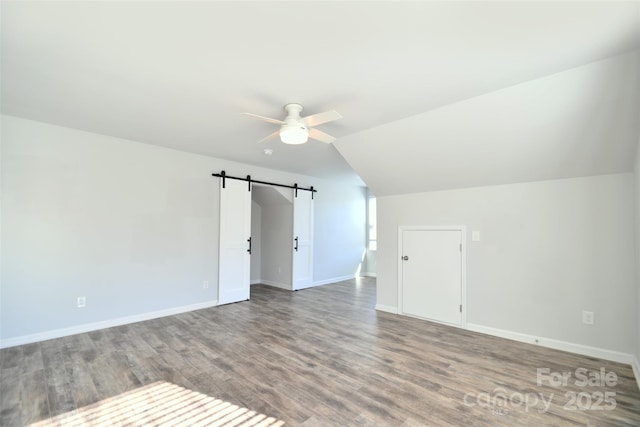 additional living space featuring ceiling fan, a barn door, lofted ceiling, and wood-type flooring