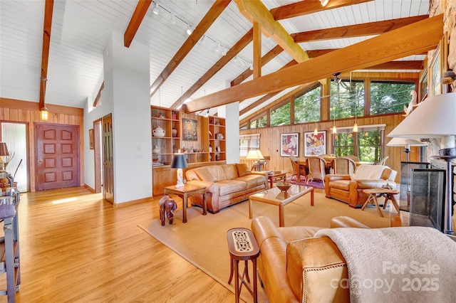 living room featuring beam ceiling, a fireplace, high vaulted ceiling, and wood walls