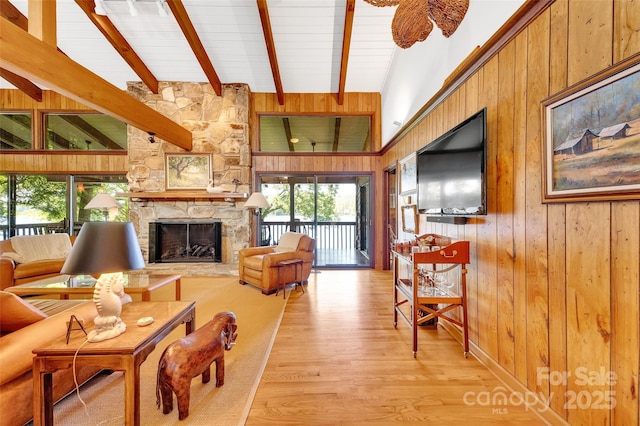 living room featuring beamed ceiling, a stone fireplace, light hardwood / wood-style floors, and wood walls