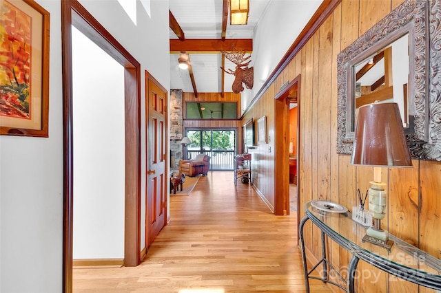 corridor featuring lofted ceiling with beams, wooden walls, and light wood-type flooring