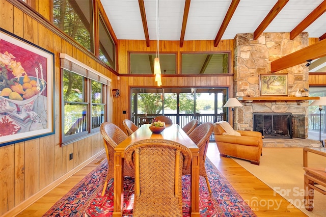 dining area featuring beam ceiling, hardwood / wood-style floors, a stone fireplace, and plenty of natural light