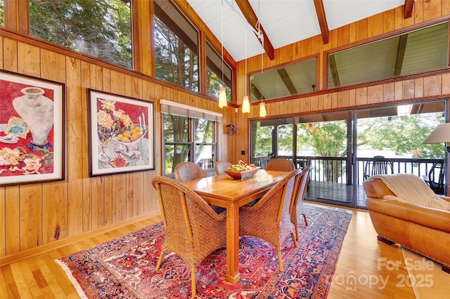 dining room featuring wood-type flooring, high vaulted ceiling, wooden walls, and beam ceiling