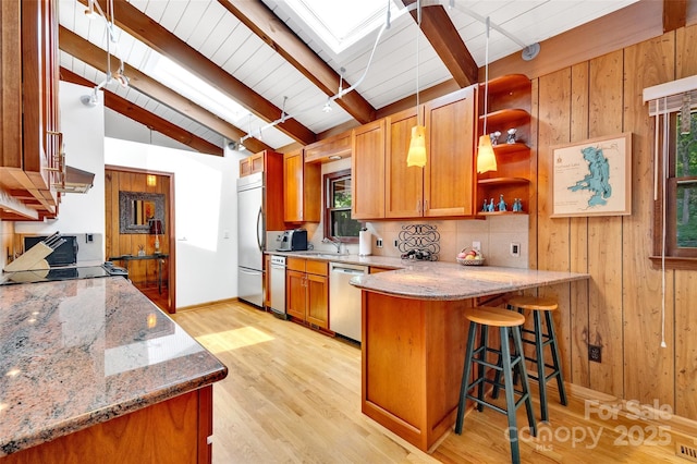 kitchen featuring vaulted ceiling with skylight, light hardwood / wood-style floors, kitchen peninsula, stainless steel appliances, and plenty of natural light