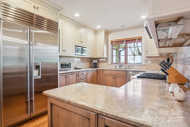 kitchen with light stone countertops, sink, cream cabinetry, and built in appliances