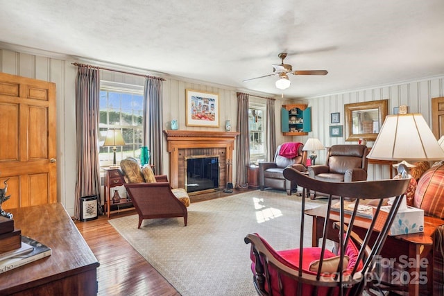 living room featuring a brick fireplace, crown molding, ceiling fan, and light wood-type flooring