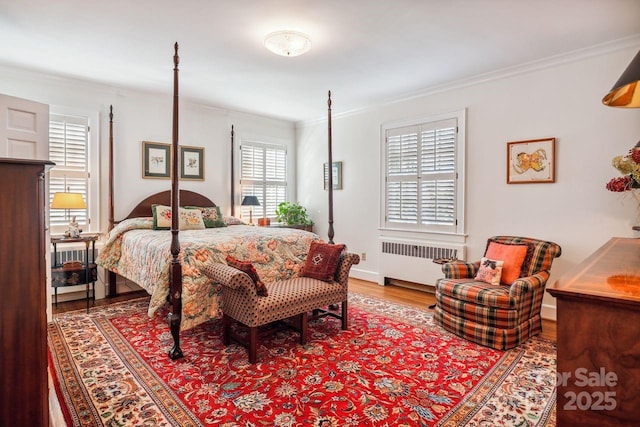 bedroom featuring wood-type flooring, radiator heating unit, multiple windows, and ornamental molding